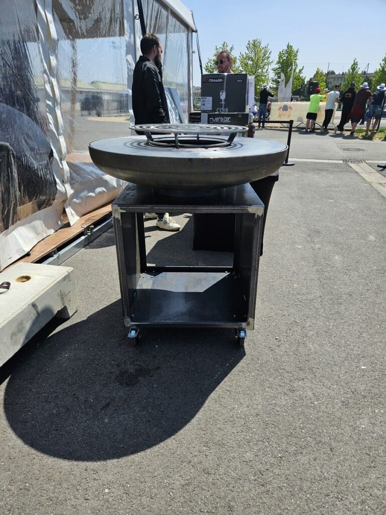 Braséro rond noir sur meuble à roulettes devant une tente d'évènement