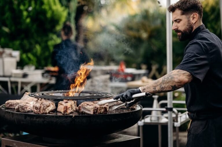 Cuisinier retournant des pièces de bœuf sur un braséro rond, en terrasse