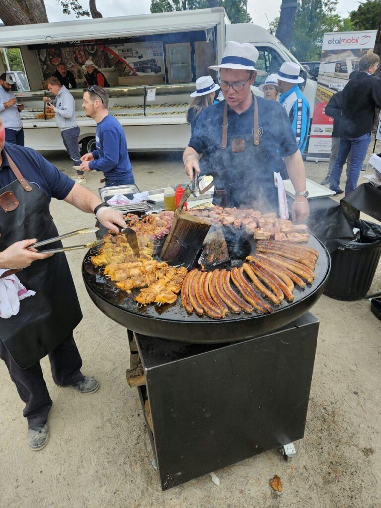 Cuisiniers en chapeau devant un braséro rond sur meuble garni de saucisses et de poulet