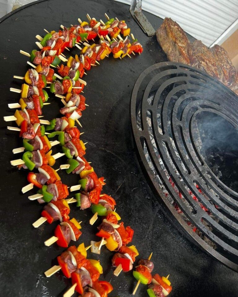 Brochettes alignées sur la plancha d'un braséro de 125, près de la grille en spirale