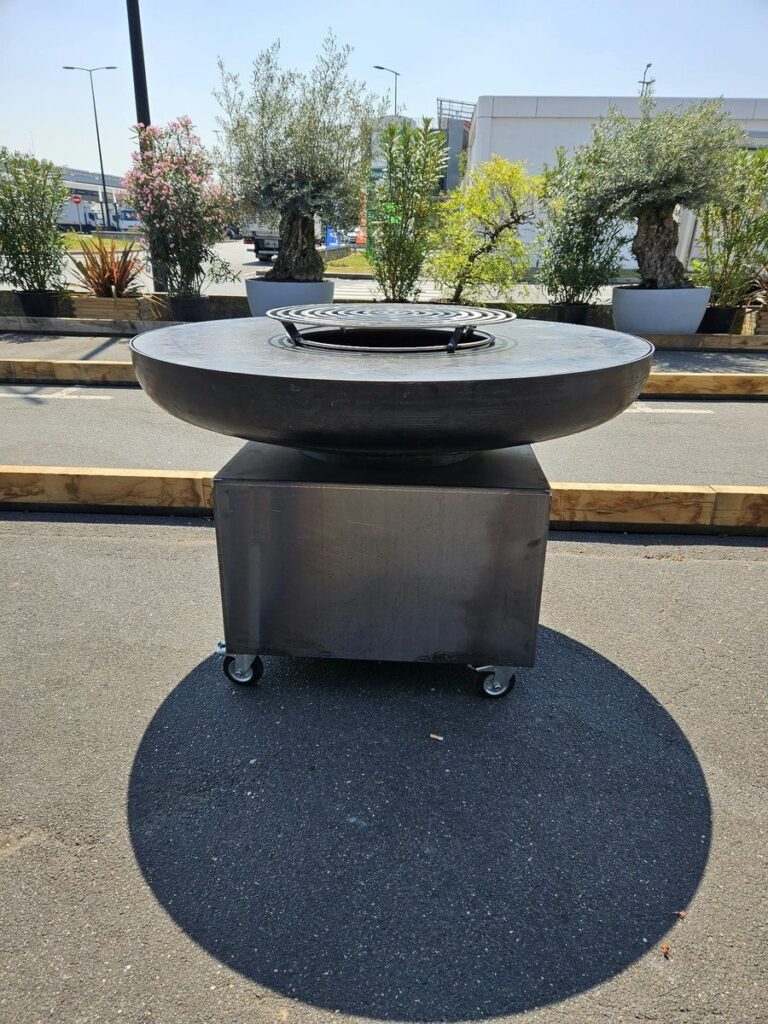Braséro rond sur meuble en inox à roulettes, posé sur un parking