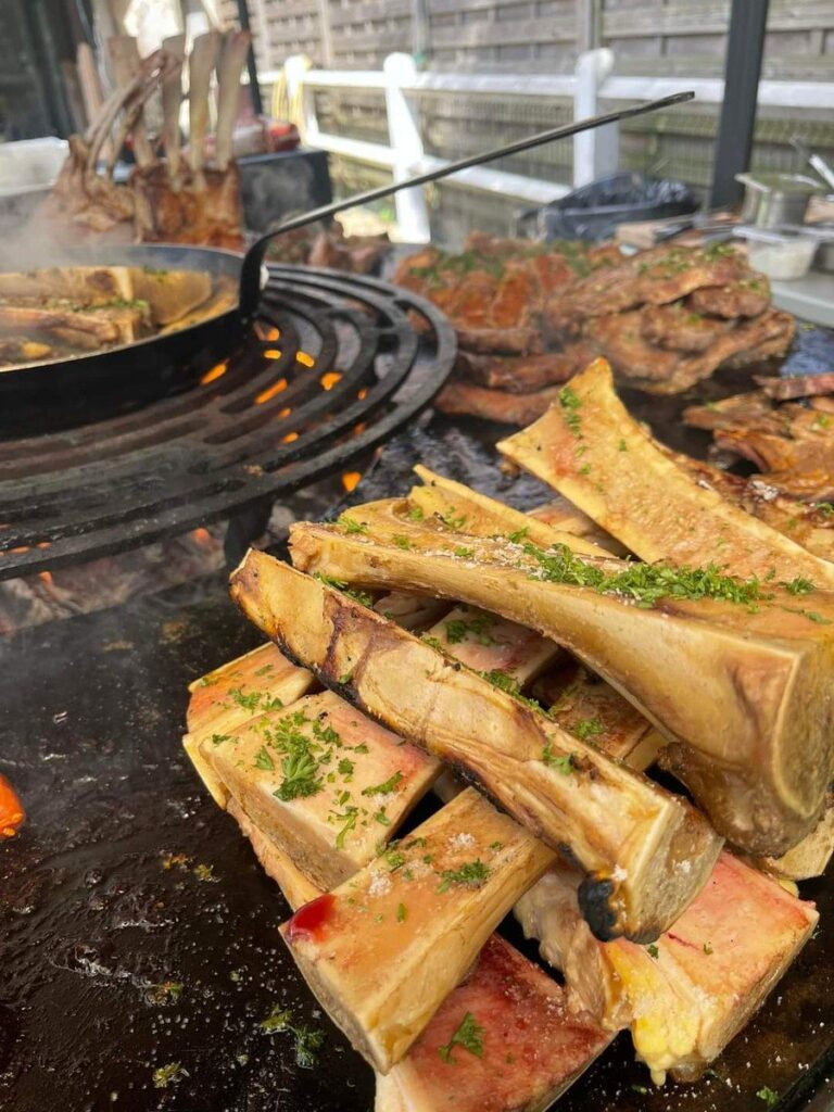 Os à moelle persillés empilés sur la plancha, poêle et côtes de bœuf au fond