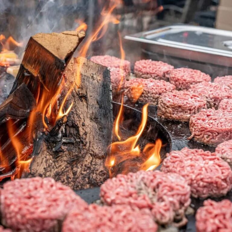 Steaks hachés autour d'une bûche enflammée sur la plancha d'un braséro de 150