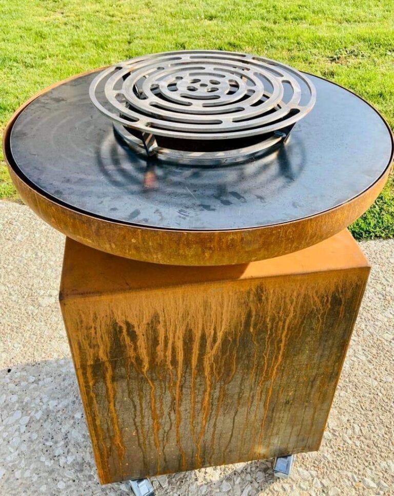 Braséro rond en acier corten sur meuble corten, posé sur une allée gravillonnée