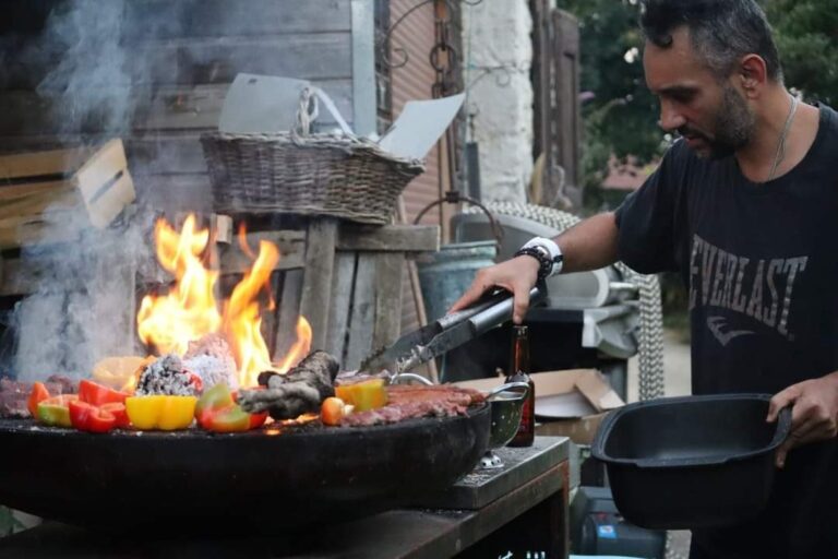 Cuisinier devant les flammes d'un braséro sur meuble garni de poivrons et de viandes