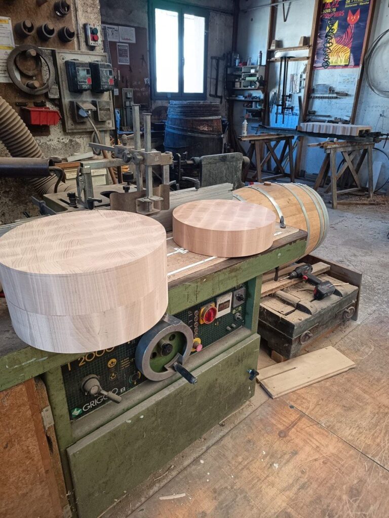 Deux billots de boucher en bois debout sur la toupie de l'atelier du tonnelier, avec une barrique au fond