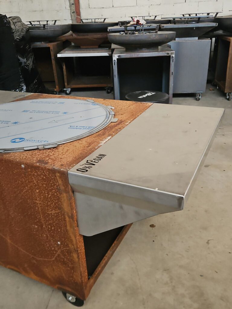 Braséro en acier corten en cours de fabrication, avec un plateau en inox sur lequel est gravé le nom « 0% Végan »