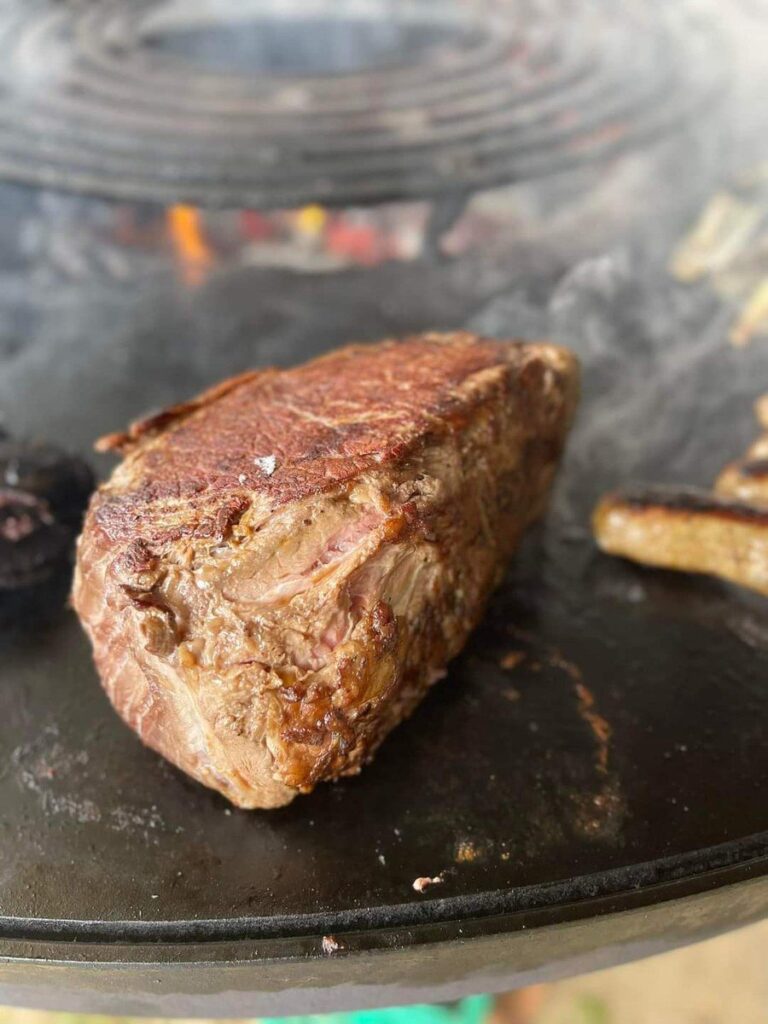 Côte de bœuf grillée en gros plan sur la plancha, grille en spirale derrière