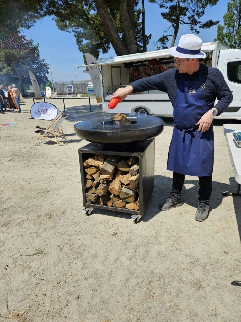 Cuisinier en chapeau panama devant un braséro sur meuble à bûches, sur une plage