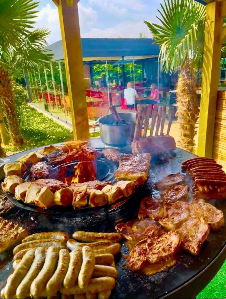 Grillades de saucisses et de côtes sur un grand braséro, palmiers et terrasse au fond