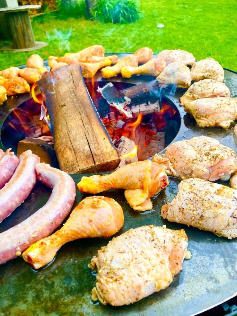 Poulet mariné et saucisses autour d'une bûche sur la plancha, pelouse au fond