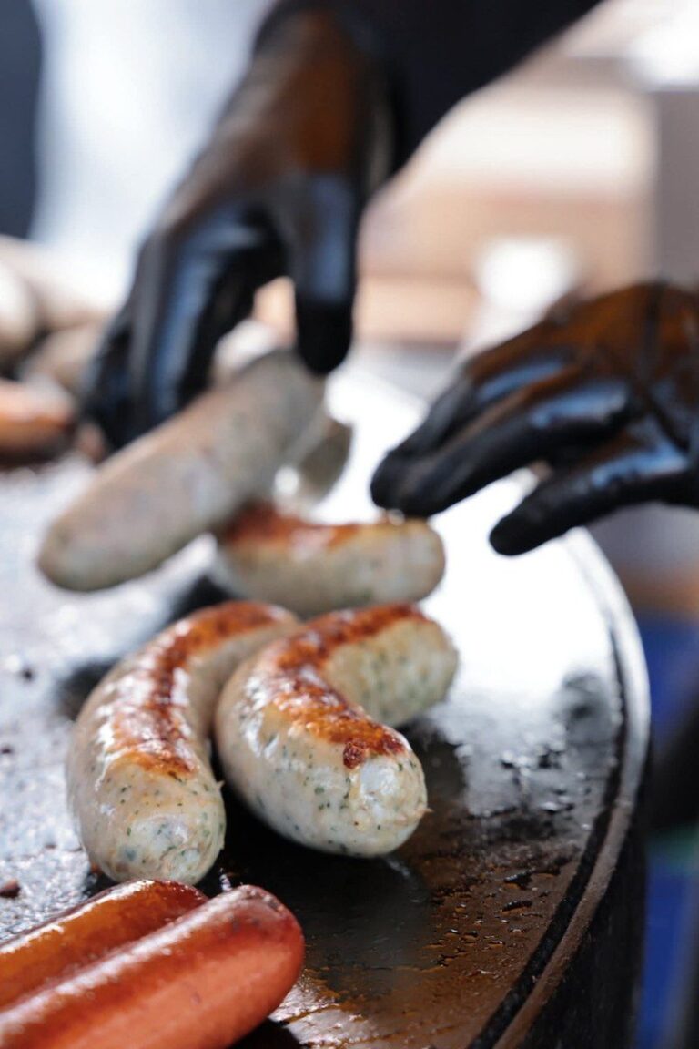 Saucisses blanches retournées avec des gants noirs sur la plancha
