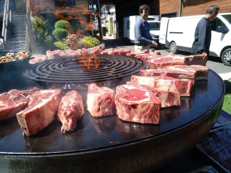 Côtes de bœuf et pièces de viande sur la plancha d'un braséro monté sur remorque, camion blanc au fond